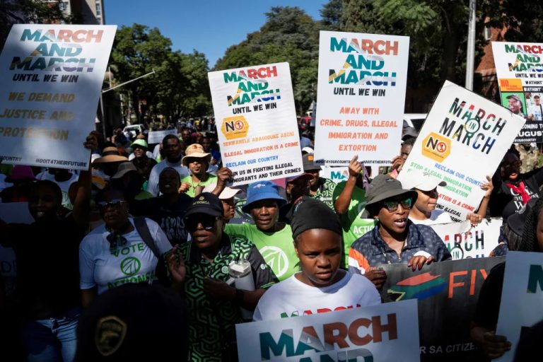 A crowd of demonstrators holding up protest signs reading March and March against illegal immigration and crime.