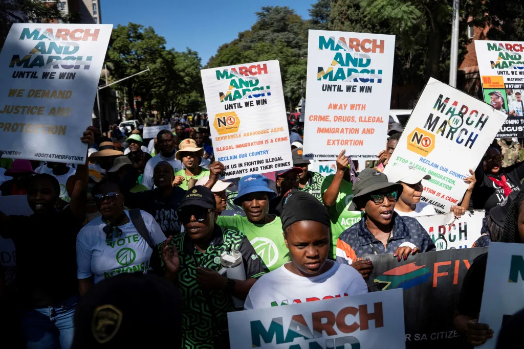 A crowd of demonstrators holding up protest signs reading March and March against illegal immigration and crime.