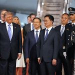 Donald Trump walking alongside international diplomats and officials on a tarmac at night, surrounded by security and government personnel.