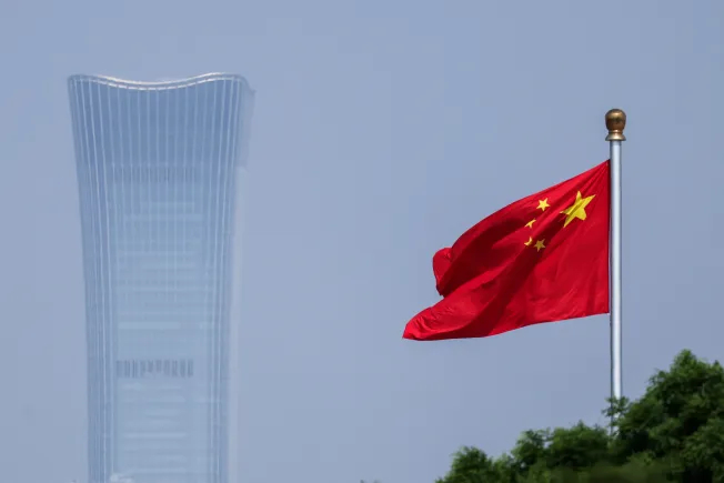 The Chinese national flag waving in the wind with a modern skyscraper in the background.