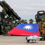 Taiwanese soldiers in camouflage standing with a large national flag next to military missile launchers and a drone.