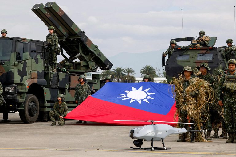 Taiwanese soldiers in camouflage standing with a large national flag next to military missile launchers and a drone.