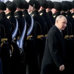 Vladimir Putin walking past a line of Russian military guards in uniform.