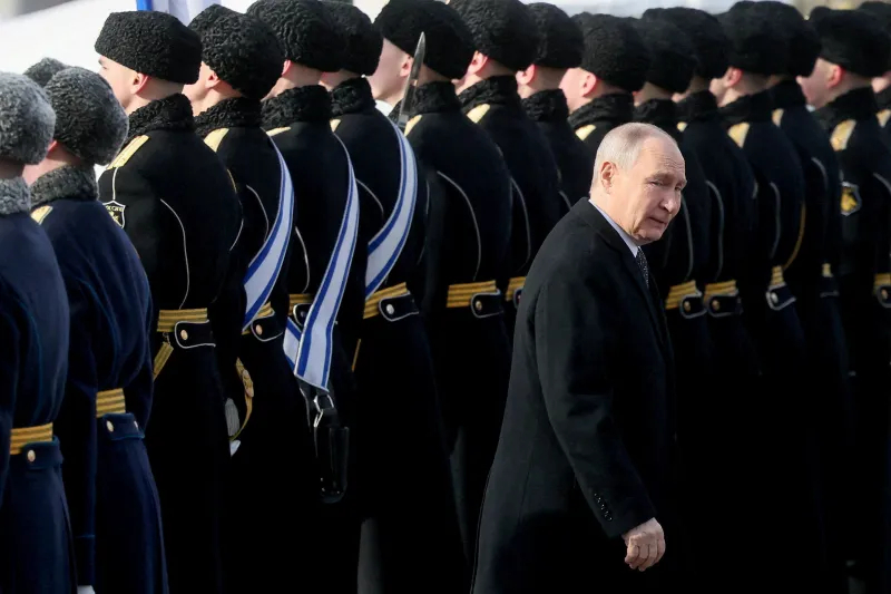 Vladimir Putin walking past a line of Russian military guards in uniform.