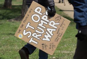 Person carrying a cardboard sign that reads "Stop Trump's War" at a protest.