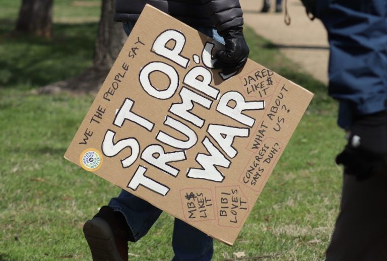 Person carrying a cardboard sign that reads "Stop Trump's War" at a protest.