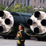 Large Chinese ballistic missile canisters on transport vehicles during a military parade with a soldier in the foreground.
