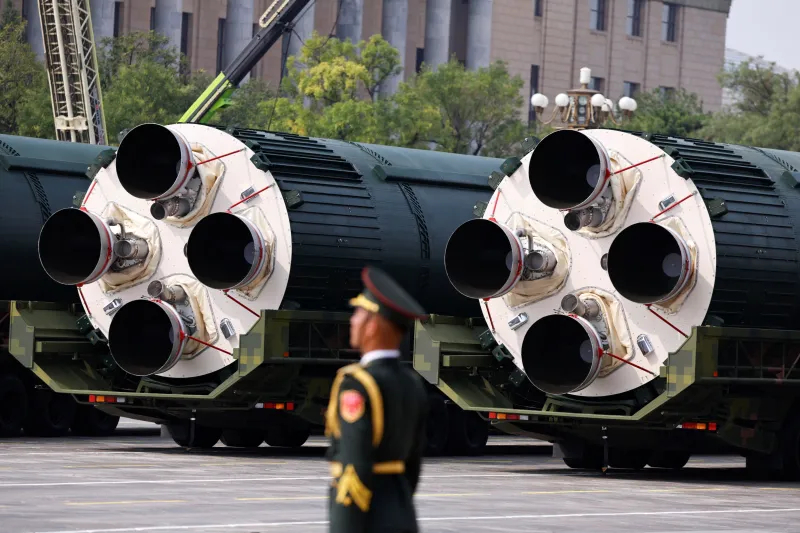 Large Chinese ballistic missile canisters on transport vehicles during a military parade with a soldier in the foreground.