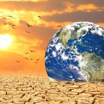 Earth globe sitting on cracked, dry desert ground at sunset.