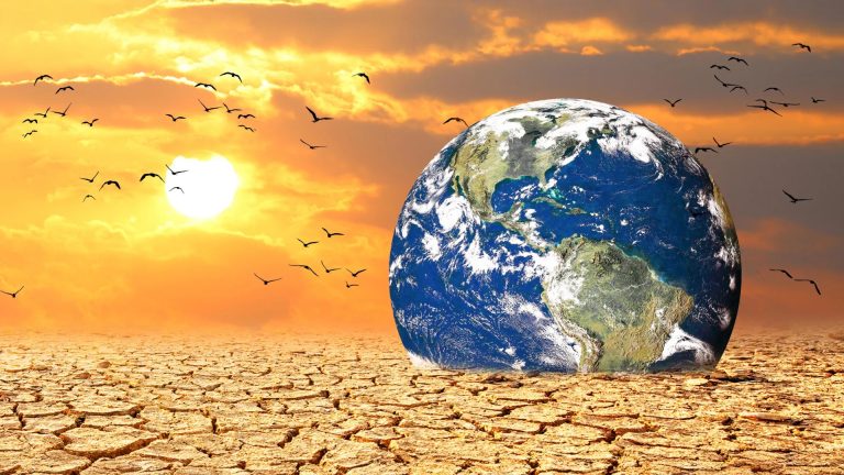 Earth globe sitting on cracked, dry desert ground at sunset.