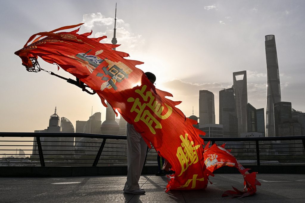 A person holding a long red dragon banner on a Shanghai waterfront with the Pudong skyline in the background.