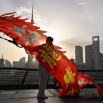 A person holding a long red dragon banner on a Shanghai waterfront with the Pudong skyline in the background.