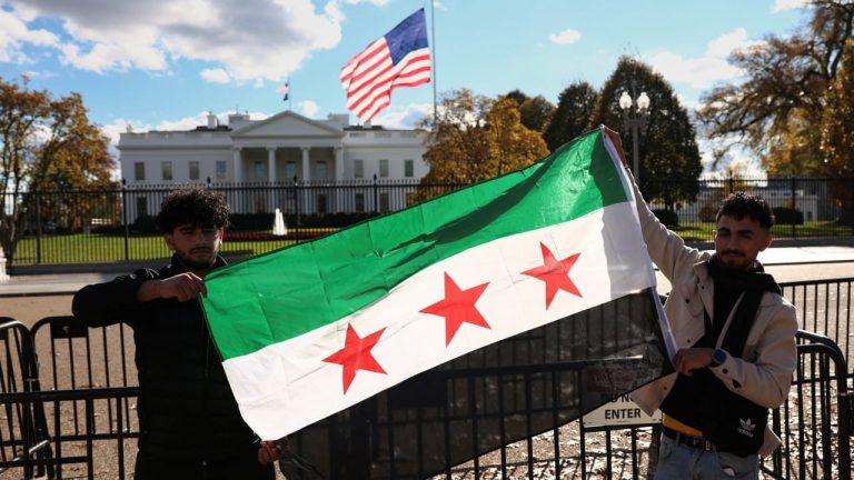 Two individuals holding the Syrian opposition flag in front of the White House.