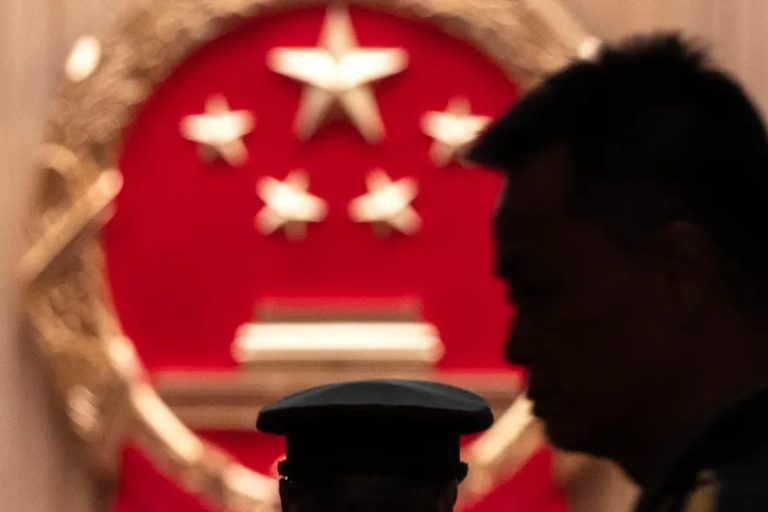 Silhouette of a Chinese military officer in front of the official emblem of the People's Republic of China.