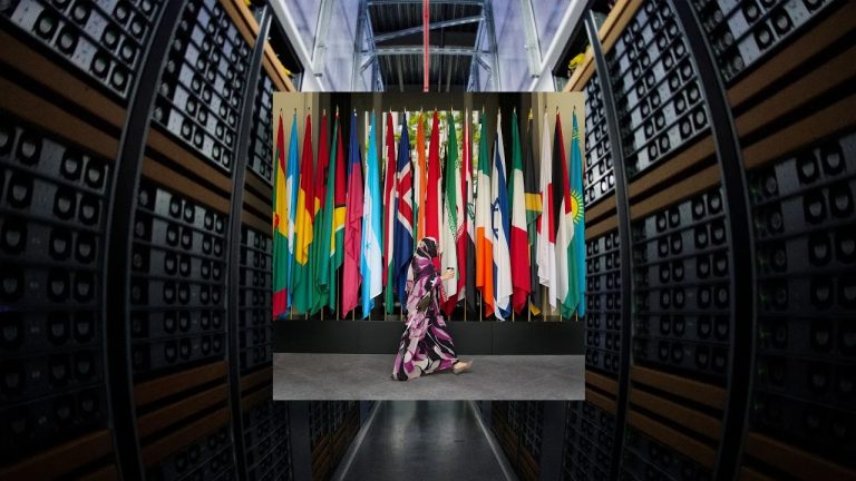 A person walking in front of a row of international flags set against a backdrop of server racks.