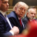 Former U.S. President Donald Trump seated at a formal meeting table.