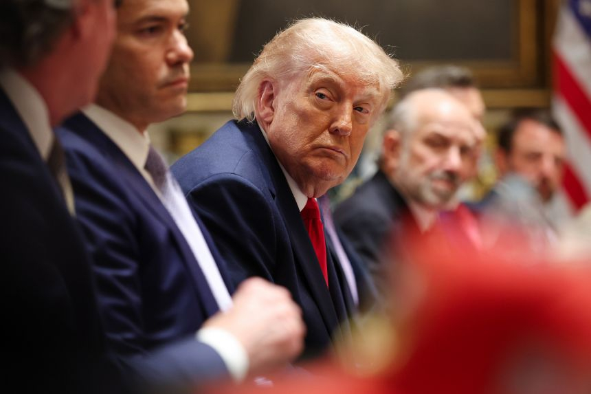 Former U.S. President Donald Trump seated at a formal meeting table.