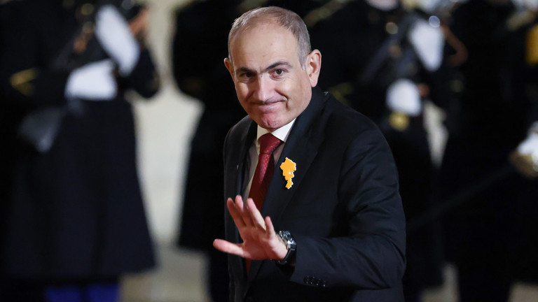 Armenian Prime Minister Nikol Pashinyan waving to the crowd while wearing an orange lapel pin.