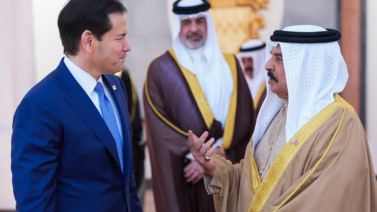 A U.S. political figure in a blue suit engaging in a formal discussion with a Bahraini official wearing traditional white thobe and ghutra.