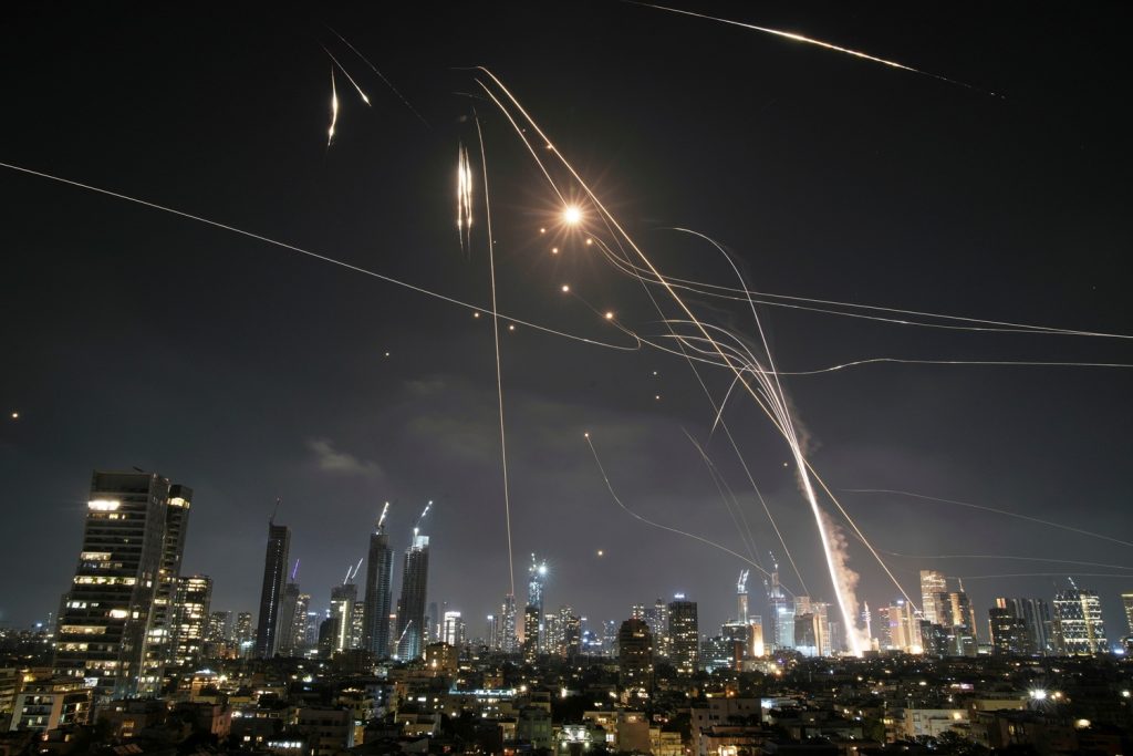 Night view of the Tel Aviv skyline illuminated by defensive missile interceptions and light trails.