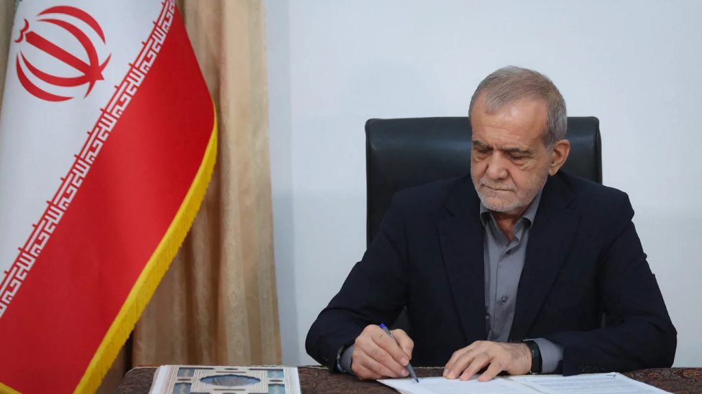 A man in a suit sitting at a desk and signing a document.