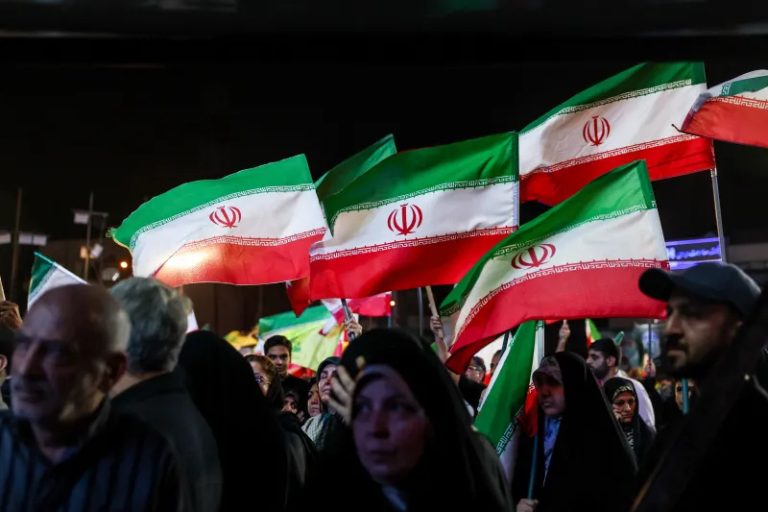 Crowd waving Iranian flags at a public gathering during a geopolitical event.