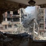 A construction vehicle clearing rubble from a damaged building as seen from inside a destroyed room.