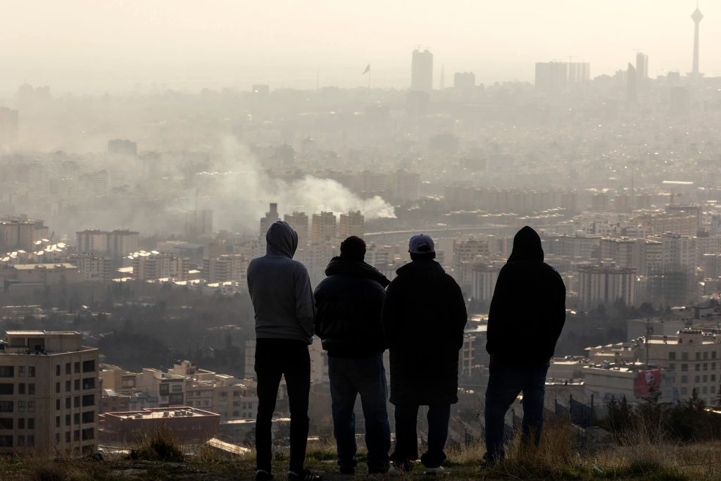 Four people standing on a hill overlooking a hazy Tehran cityscape.