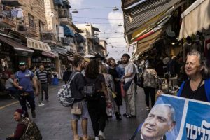 A street scene in an Israeli market with a person holding a political campaign sign featuring Benjamin Netanyahu.