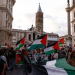 A crowd of people marching through a city street while carrying large Palestinian flags.