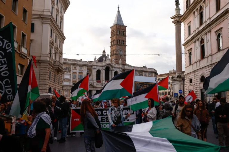 A crowd of people marching through a city street while carrying large Palestinian flags.
