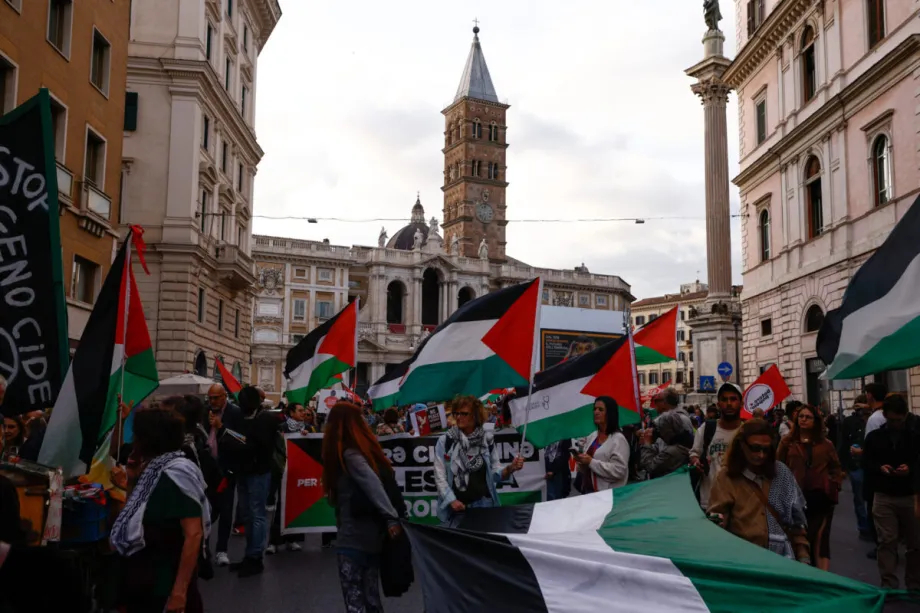 A crowd of people marching through a city street while carrying large Palestinian flags.