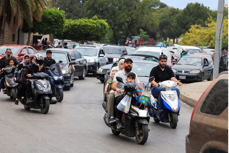 Families and civilians riding motorbikes and driving cars in heavy street traffic.