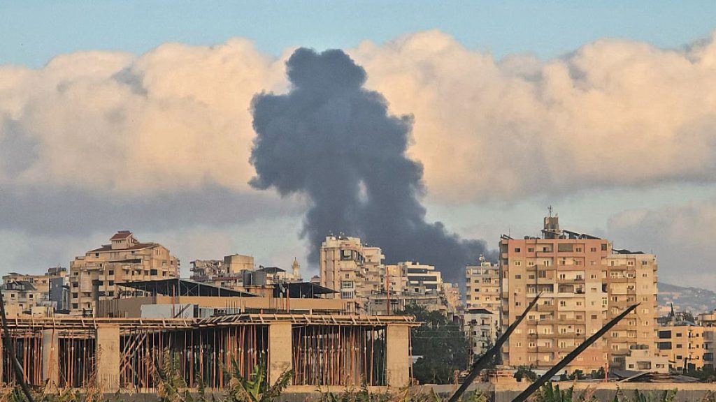 Thick black smoke rising into the sky over a Lebanese city with residential buildings in the foreground.