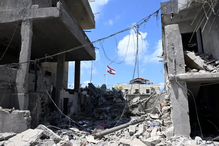 A view of a destroyed building in Lebanon with a national flag flying in the background.