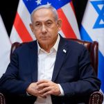Israeli Prime Minister Benjamin Netanyahu sitting in front of Israeli and American flags.