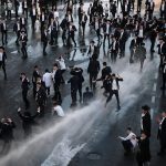An overhead view of Israeli police using a water cannon on a crowd of Orthodox Jewish protesters in a city street.