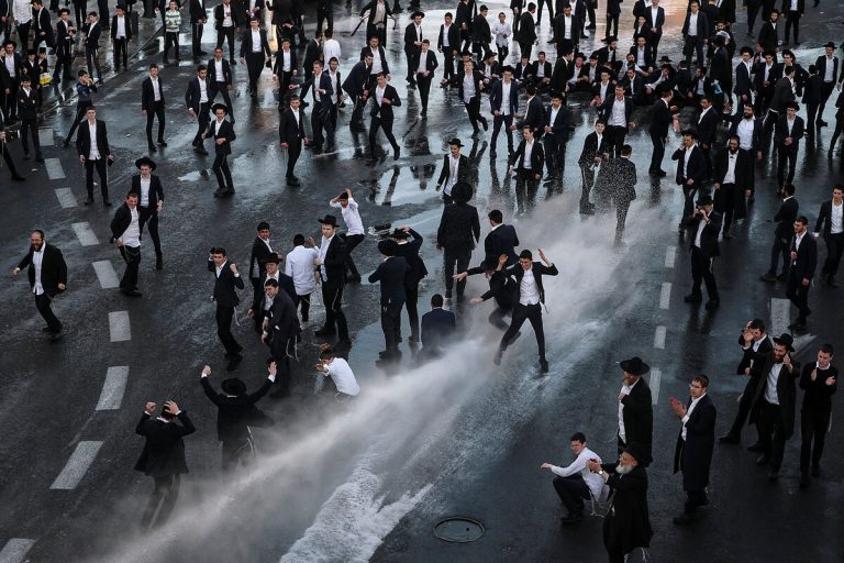 An overhead view of Israeli police using a water cannon on a crowd of Orthodox Jewish protesters in a city street.
