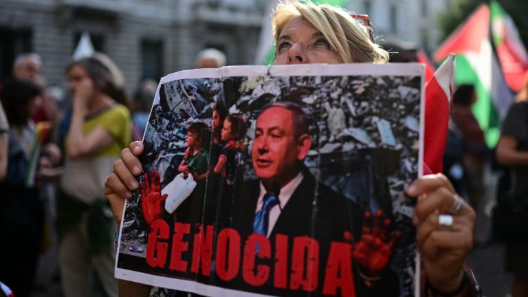 A protester holding a sign with a photo of Benjamin Netanyahu and the word "Genocida."