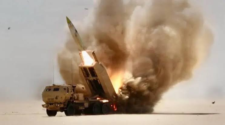 A mobile launcher firing a missile in a desert environment, surrounded by a large cloud of dust and fire.