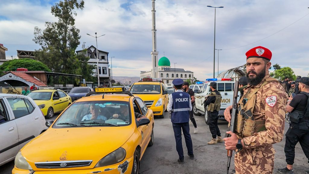A soldier in military uniform standing guard near a mosque and city traffic.