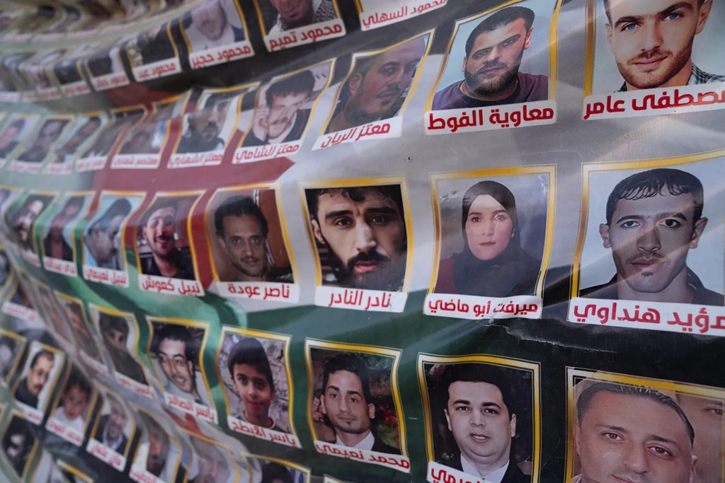 A memorial poster displayed in public featuring rows of photos of missing people in Syria.