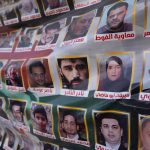 A memorial poster displayed in public featuring rows of photos of missing people in Syria.