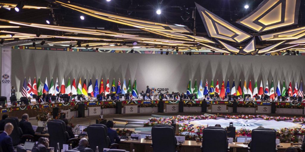 A wide view of a G20 summit conference hall featuring flags and representatives from various nations.