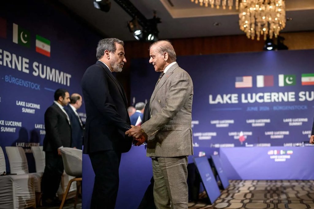 Two diplomats shaking hands at the Lake Lucerne Summit with flags of different nations displayed in the background.