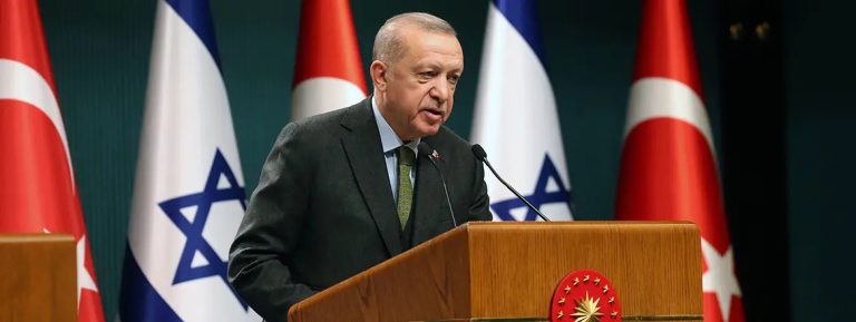 Turkish President Recep Tayyip Erdoğan speaking at a podium with Turkish and Israeli flags in the background.