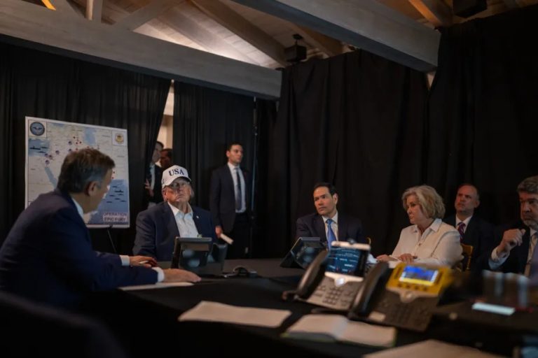 Donald Trump wearing a "USA" cap sitting at a table during a strategic briefing with advisors.