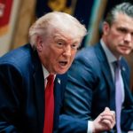 Donald Trump speaking at a conference with an associate nearby.