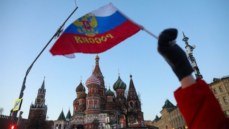 A person waving a Russian flag in front of Saint Basil's Cathedral in Moscow.