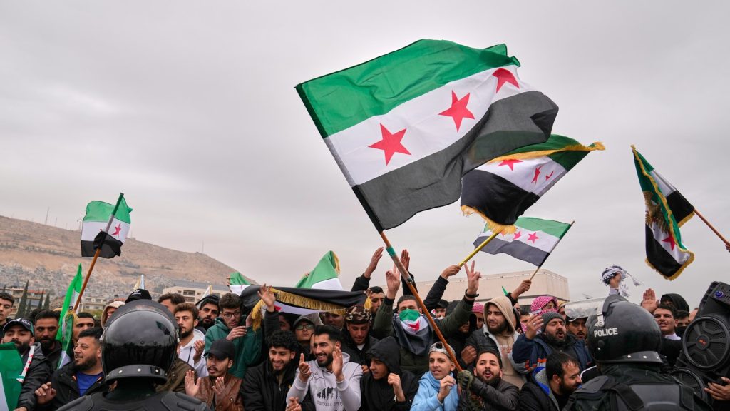 A crowd of protesters in Syria waving opposition flags in front of police officers.